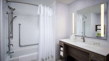 Un bagno moderno con cabina doccia, maniglioni, uno specchio grande e un mobile lavabo con spazio per gli asciugamani.