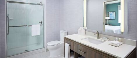 Un baño moderno con cabina de ducha de vidrio, inodoro, lavabo con tocador y un espejo grande.
