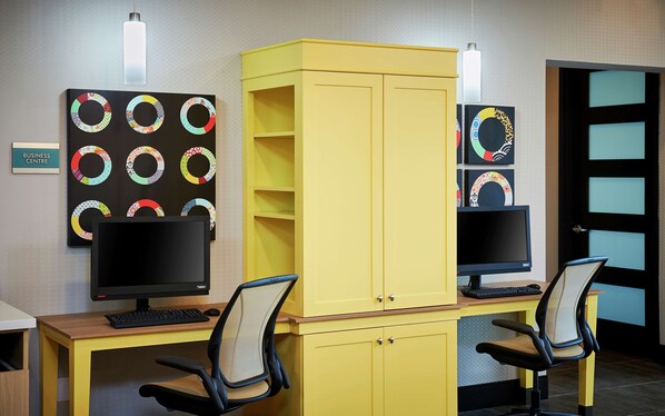 A workspace with two desks, each with a computer monitor, keyboard, and office chair. There is a yellow cabinet between the desks. - Home2 Suites by Hilton Brantford (Brantford)