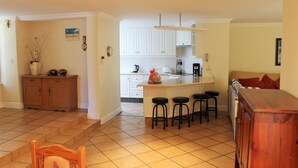 A kitchen with white cabinets, a wooden island with stools, and a dining area with a wooden table and chairs. - River Club 4213 (Plettenberg Bay)