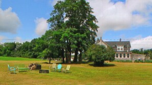 Un gran árbol en un campo cubierto de hierba, con una casa al fondo.