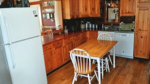 Una cocina con armarios de madera, un refrigerador blanco, una mesa de comedor de madera con sillas y un lavavajillas.