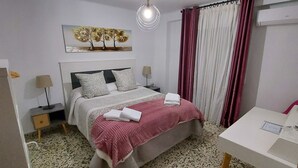 Une chambre à coucher avec un lit, des tables de chevet, une lampe, un miroir, un tableau et une fenêtre avec des rideaux.