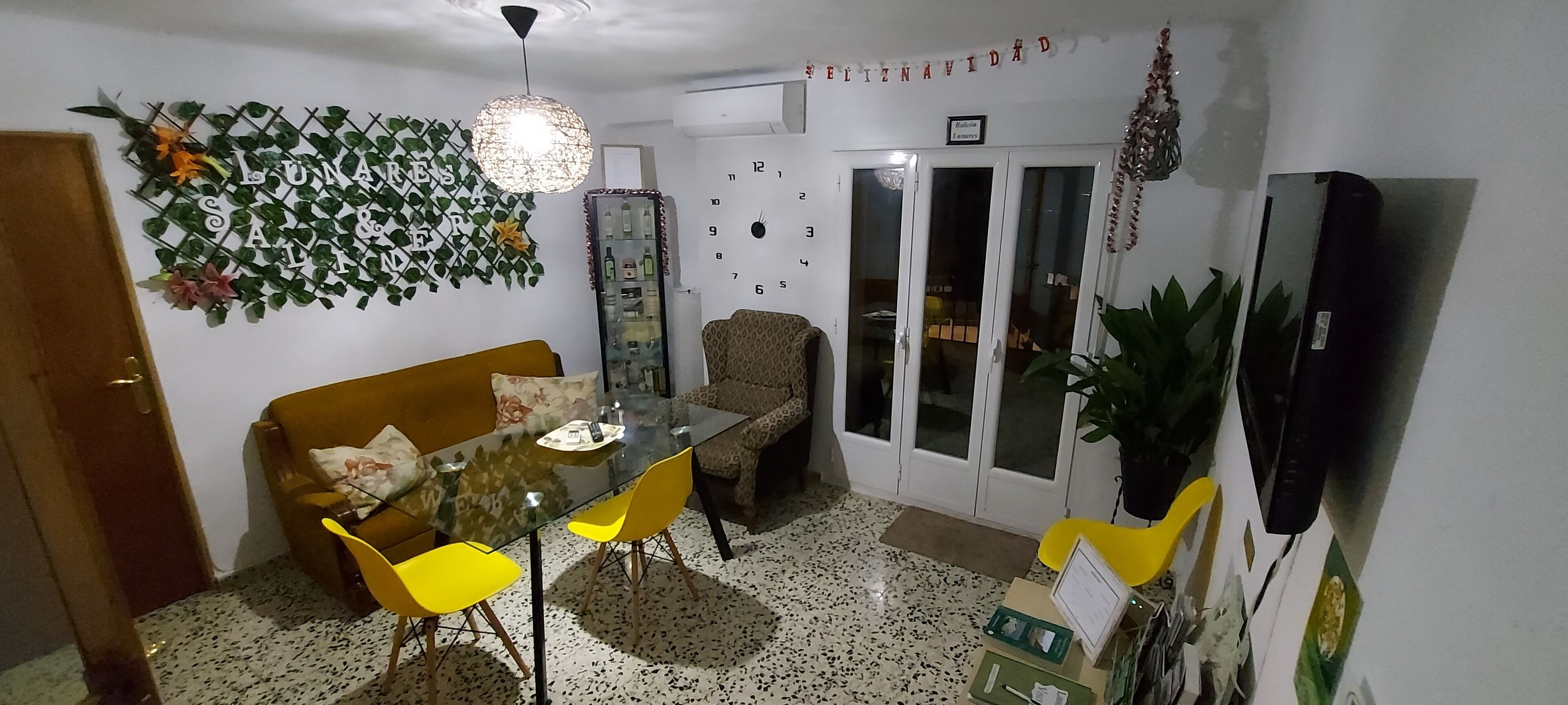 Un coin repas avec une table en verre, des chaises jaunes, un canapé et un mur décoratif.