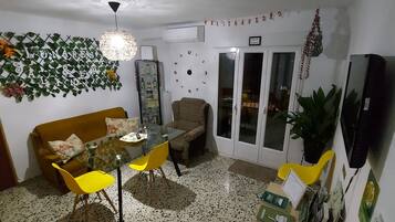 Un coin repas avec une table en verre, des chaises jaunes, un canapé et un mur décoratif.