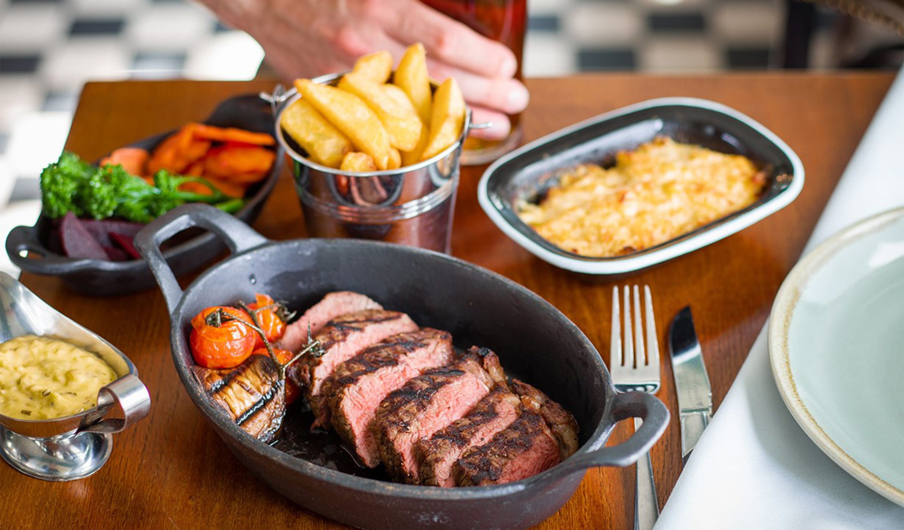 Ein Essen mit Steak, Pommes und Gemüse auf einem Holztisch.