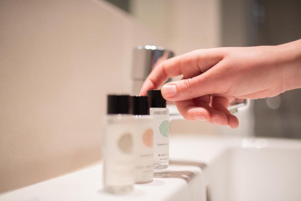 A hand reaching for a bottle with a black cap on a bathroom counter.