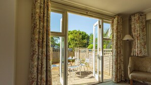 A room with a sofa, a table, and chairs, a sliding glass door leading to an outdoor area with a fence and greenery. - Thorpeness Golf Club and Hotel (Leiston)