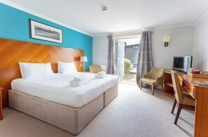 A hotel room with a large bed, a desk, a chair, a television, and a window with curtains. - Thorpeness Golf Club and Hotel (Leiston)