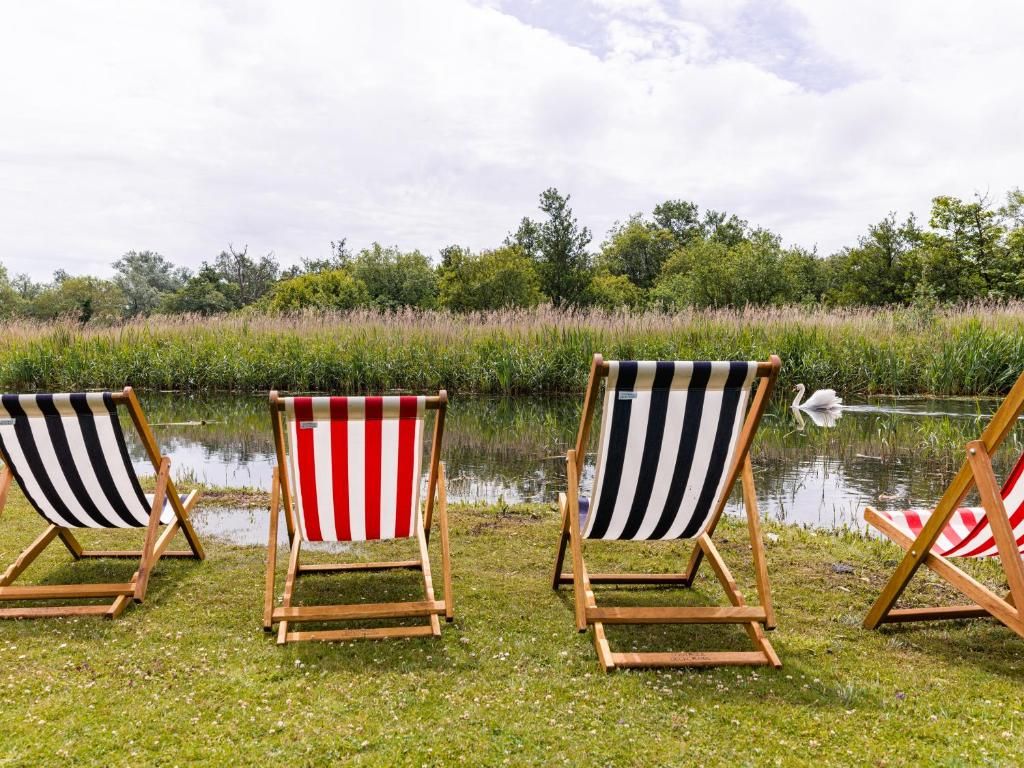 Three beach chairs with striped cushions by a calm body of water, surrounded by greenery.