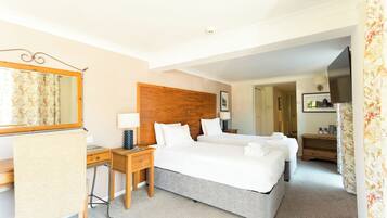 Quarto de hotel com cabeceira de madeira, duas camas, escrivaninha com cadeira, espelho e televisão.