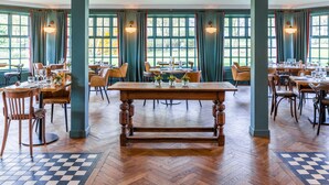A spacious dining area with wooden tables and chairs, large windows with curtains, and a herringbone floor pattern. - Thorpeness Golf Club and Hotel (Leiston)