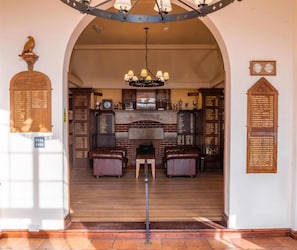 An arched entrance with a wooden signboard, a fireplace, leather seating, and a chandelier.