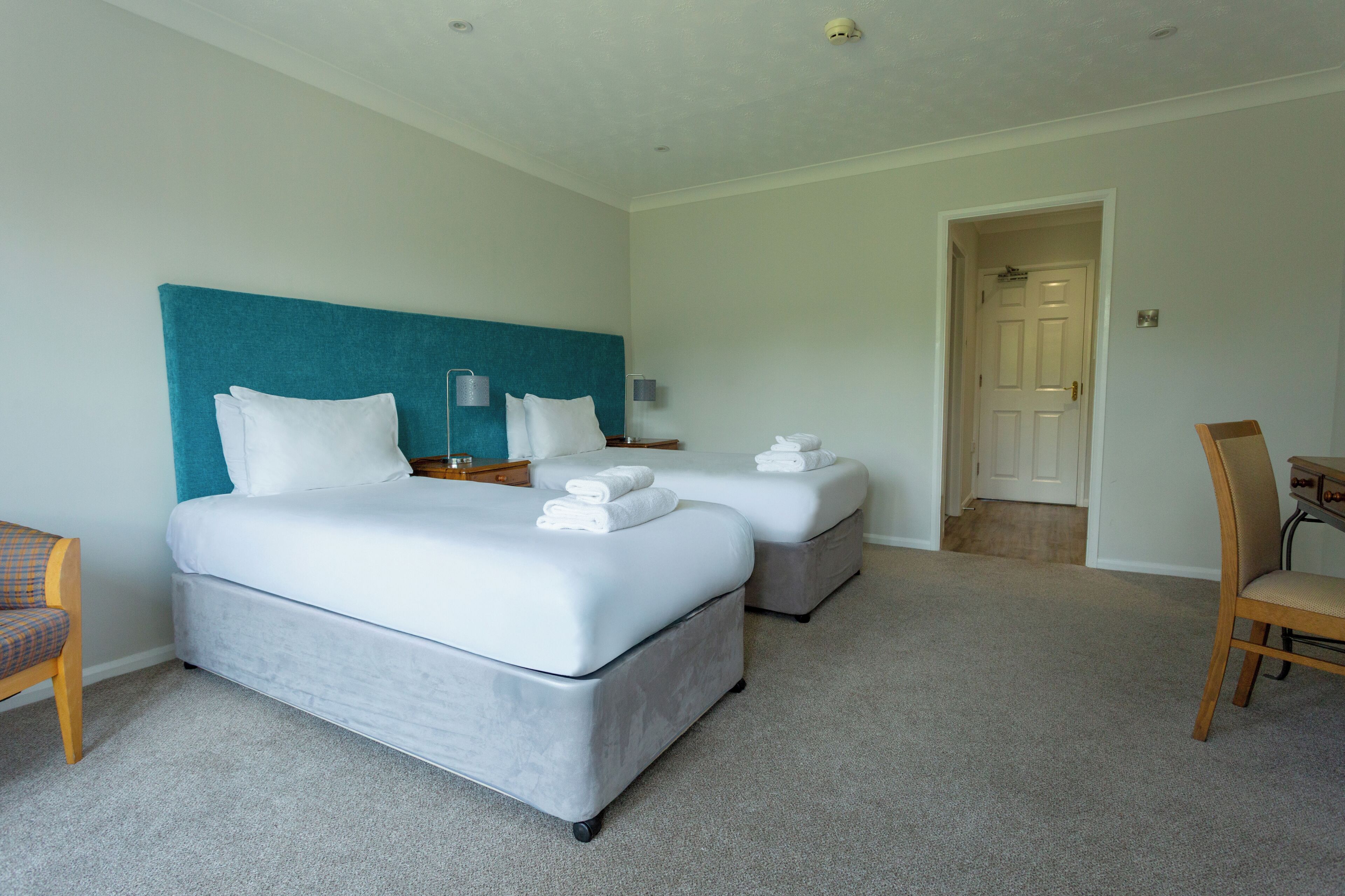 A hotel room with two beds, a desk, a chair, and a door.