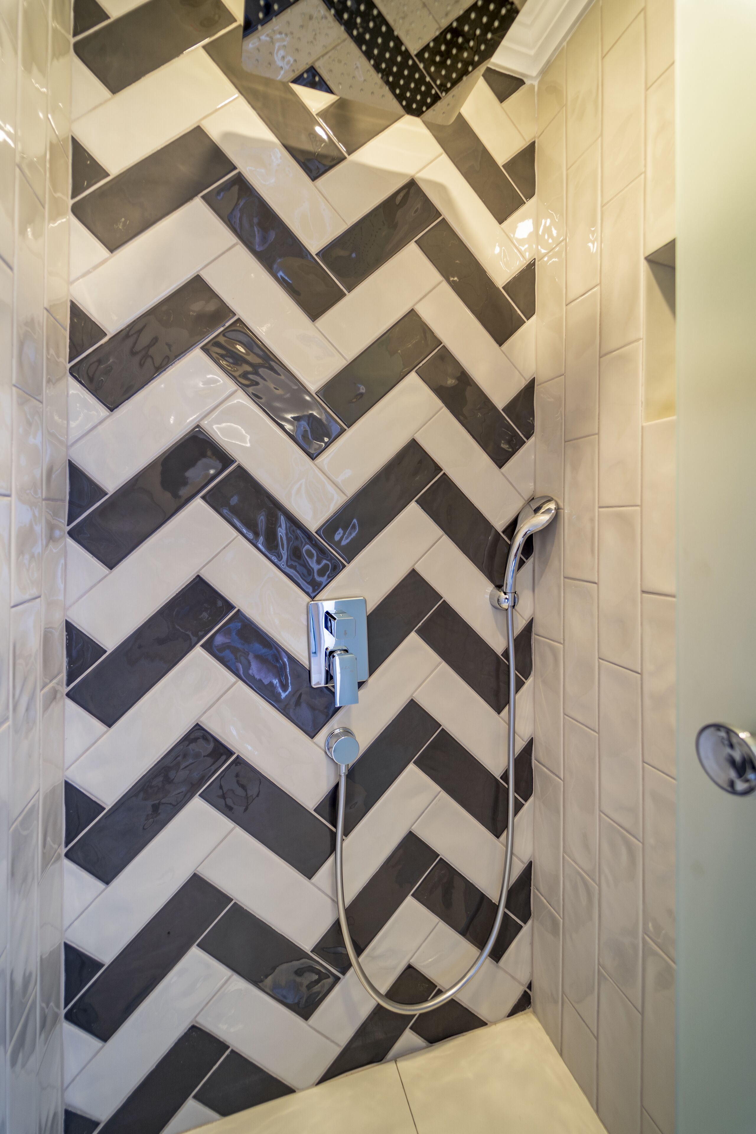Une douche avec un carrelage à motifs chevrons noir et blanc, une douchette à main et un panneau de commande fixé au mur.