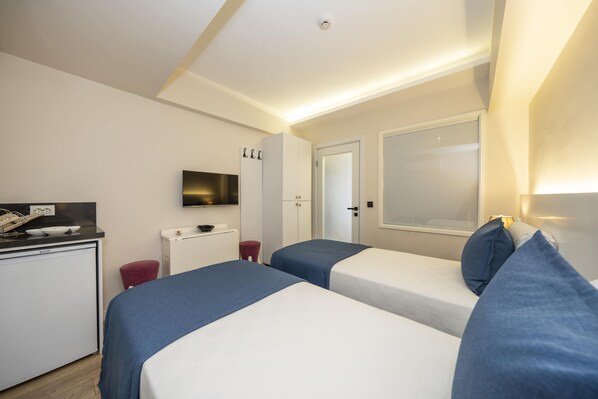 Una habitación de hotel compacta con dos camas, una kitchenette pequeña, un televisor y una ventana con persianas.