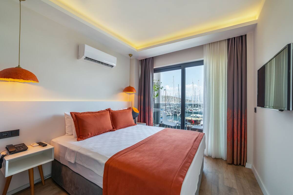 A hotel room with a bed, bedside table, and a view of the marina.