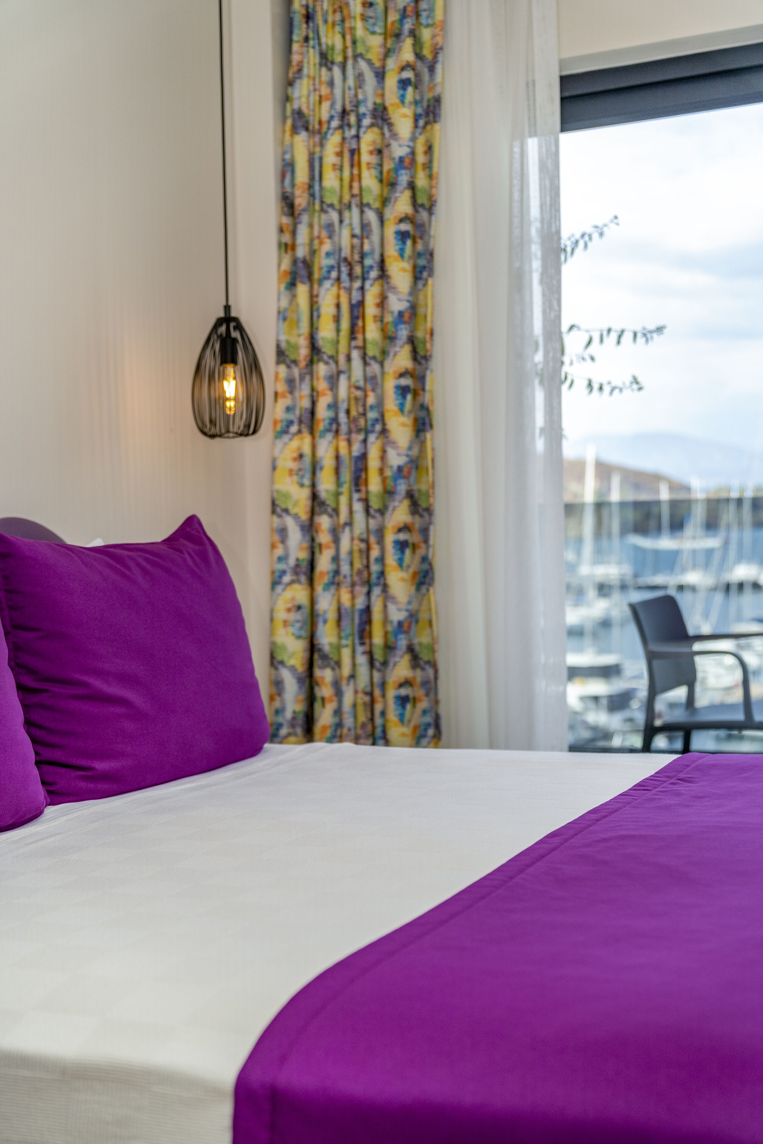 A bed with a purple bedspread, a purple pillow, and a hanging light fixture.