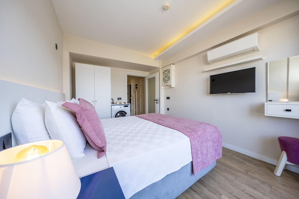 A modern hotel room with a bed, a desk, a TV, and an air conditioning unit. - Ece Marina Suites (Fethiye)