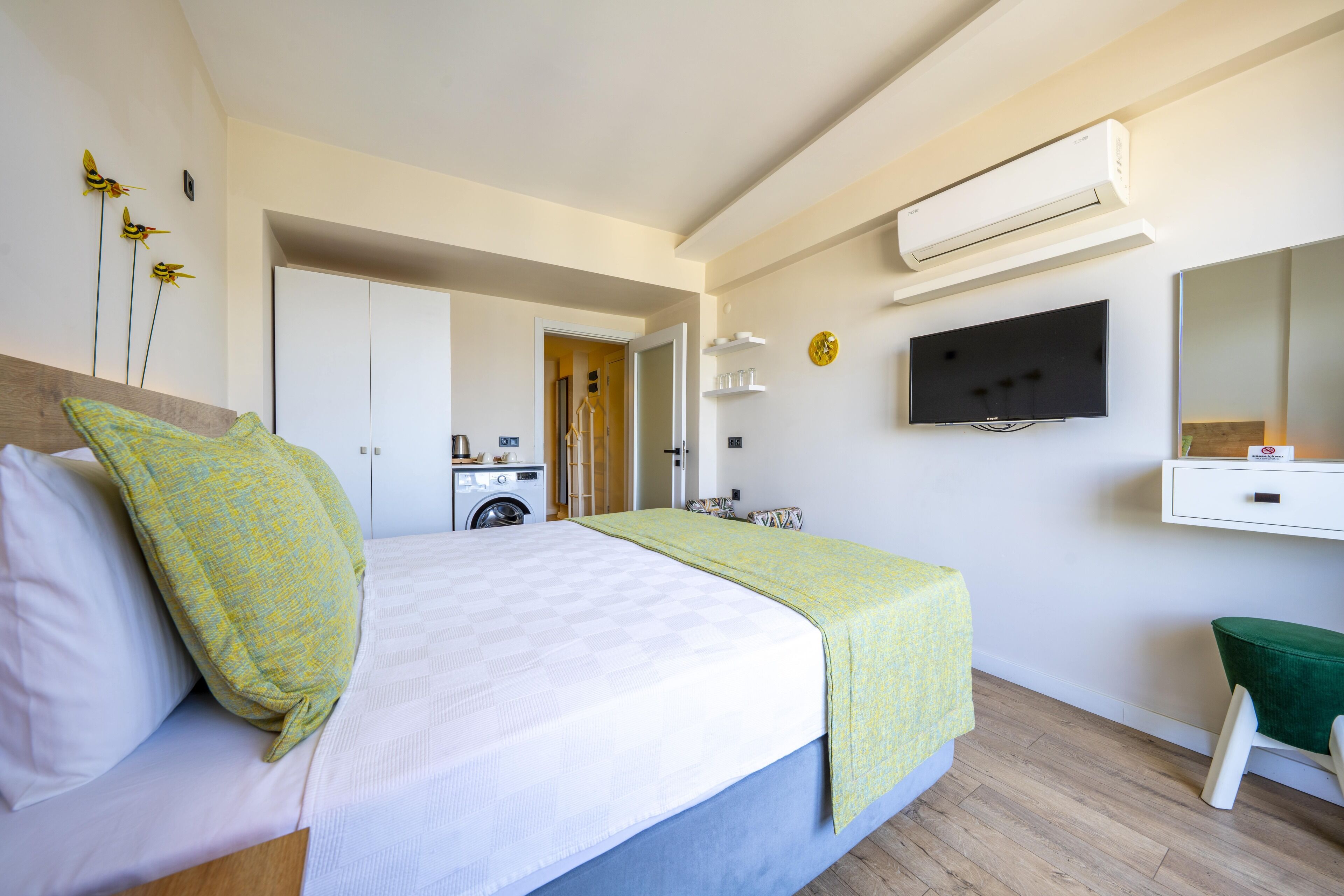 A bedroom with a bed, a washing machine, a TV, and an air conditioner.