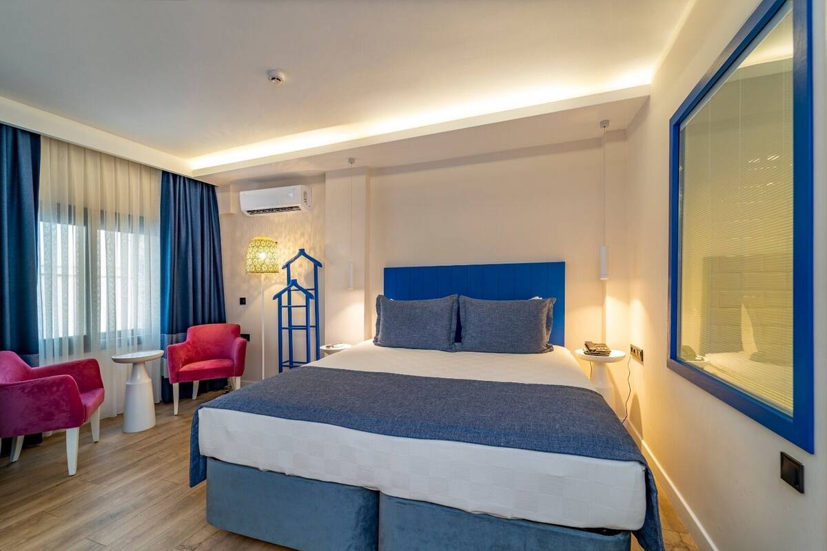 A modern hotel room with a large bed, a red armchair, a small table, and a blue headboard.