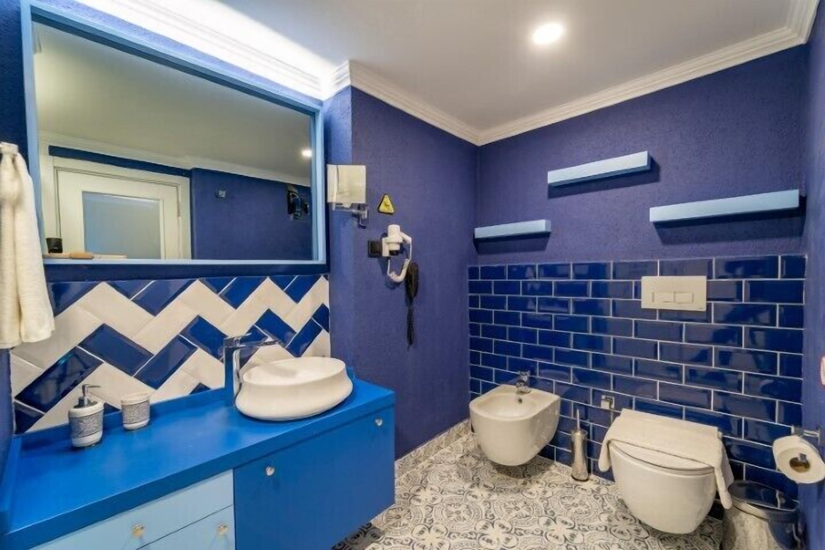 A bathroom with a blue and white tile backsplash, a white sink, a bidet, and a toilet.