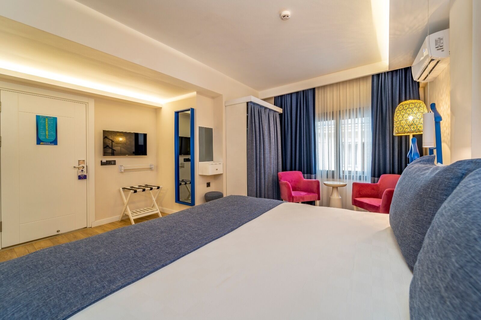 Ein Hotelzimmer mit Bett, Fernseher, Spiegel, Schreibtisch und einem Fenster mit Vorhängen.