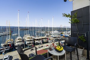 Un balcón con una mesa, sillas y una planta en maceta, con vistas a un puerto deportivo lleno de veleros.