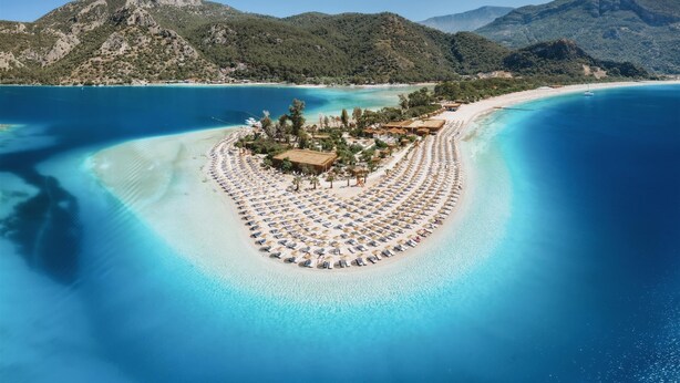 An aerial view of a resort island with a circular layout of sunbeds and a central building surrounded by trees. - Ece Marina Suites (Fethiye)