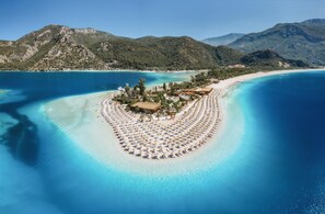 An aerial view of a resort island with a circular layout of sunbeds and a central building surrounded by trees. - Ece Marina Suites (Fethiye)