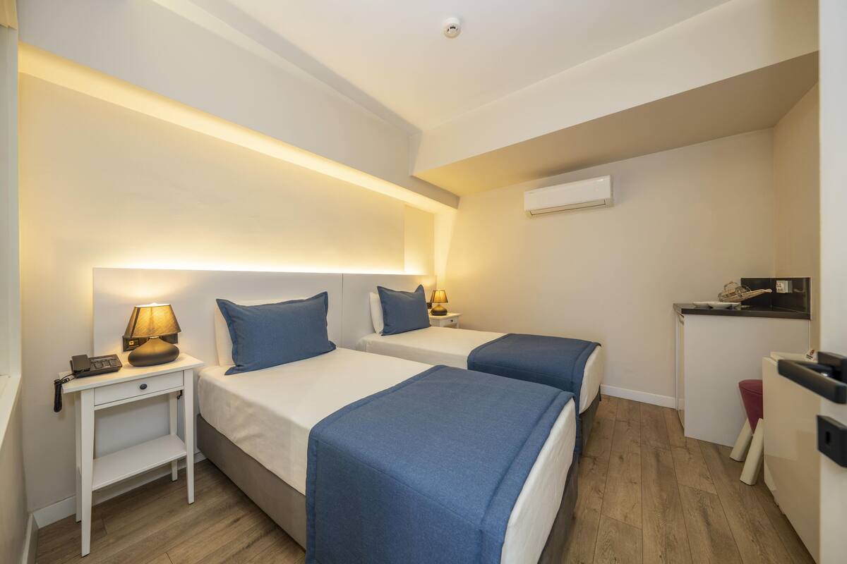A hotel room with two beds, a desk, a lamp, and a small kitchenette.