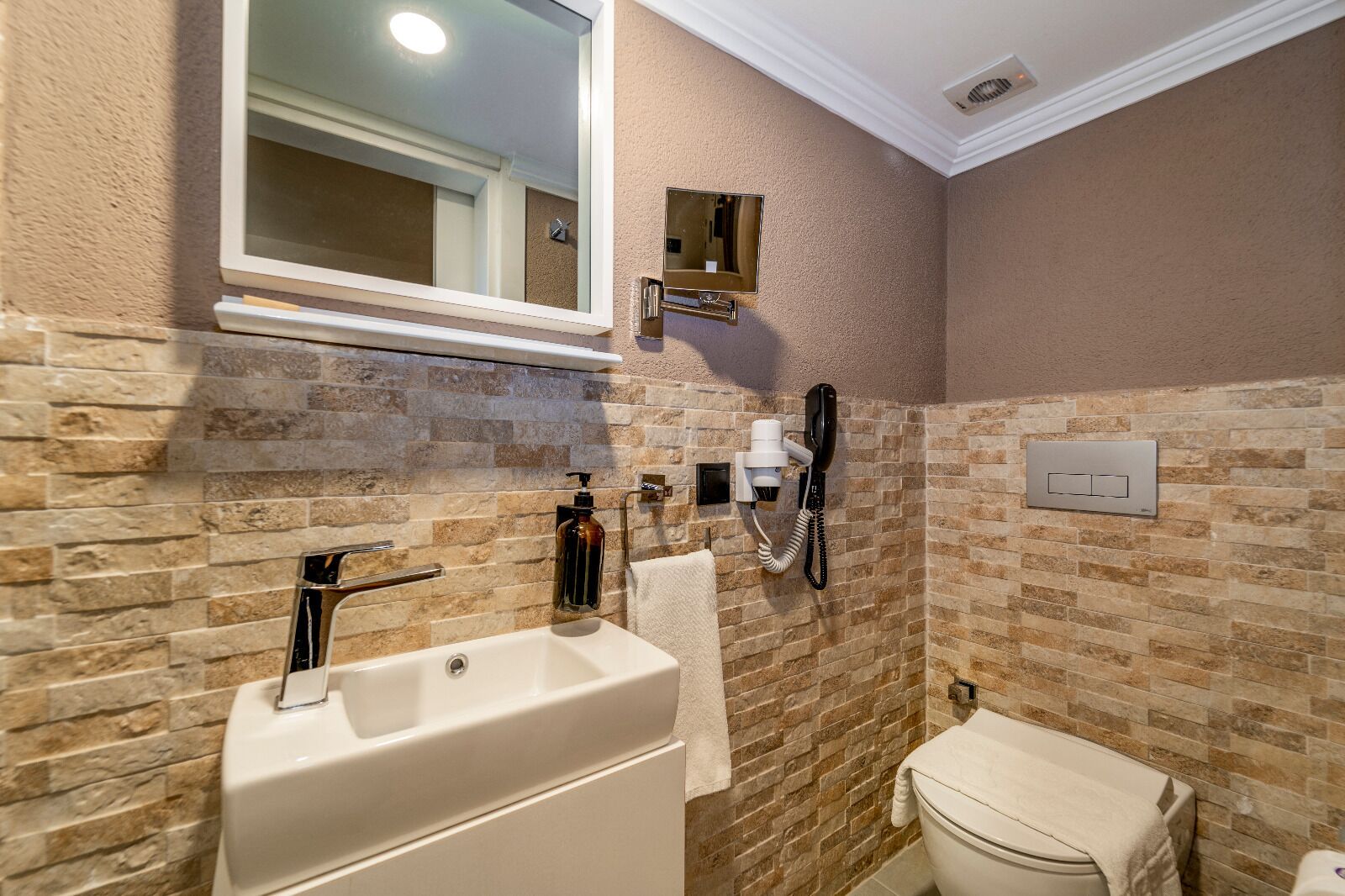 Een badkamer met een stenen muur, een witte badkuip, een toilet, een spiegel en een telefoon.