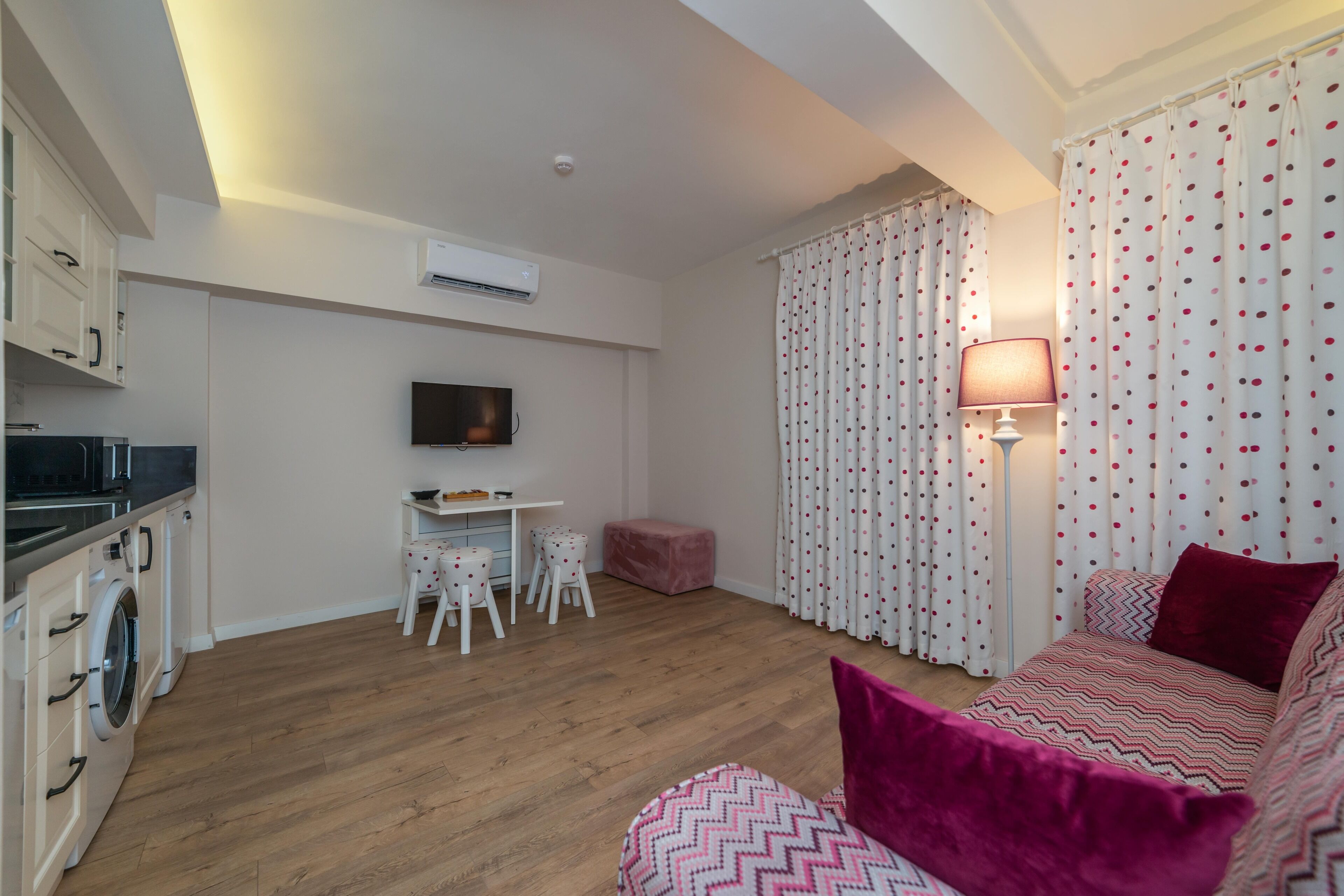 A compact living space with a kitchenette, a TV, a dining area, and a bedroom with a bed and curtains.