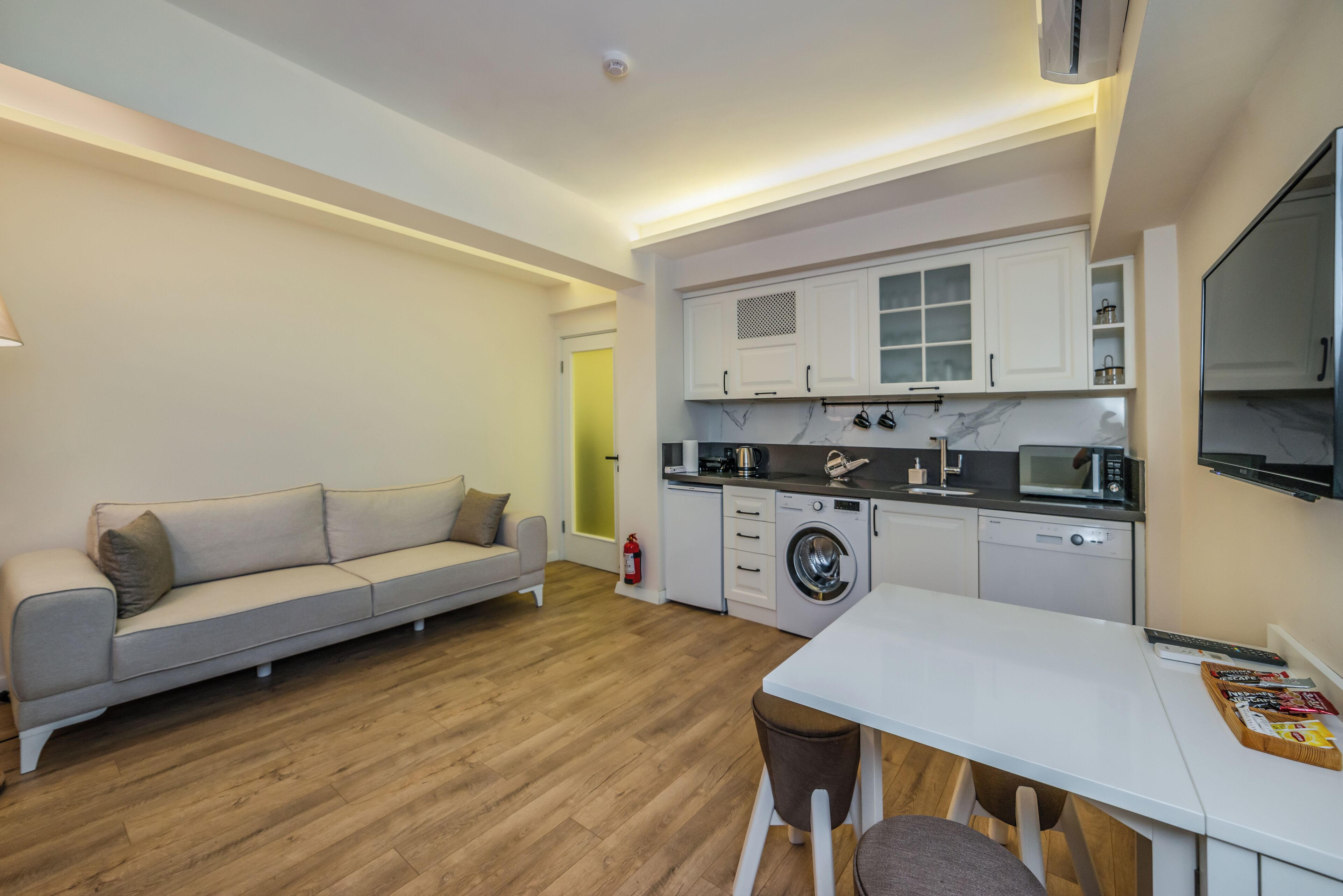 A compact living space with a kitchenette, a sofa, a dining table, and a washing machine.