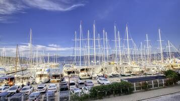 A marina with numerous sailboats docked, a parking area with cars, and a clear blue sky.