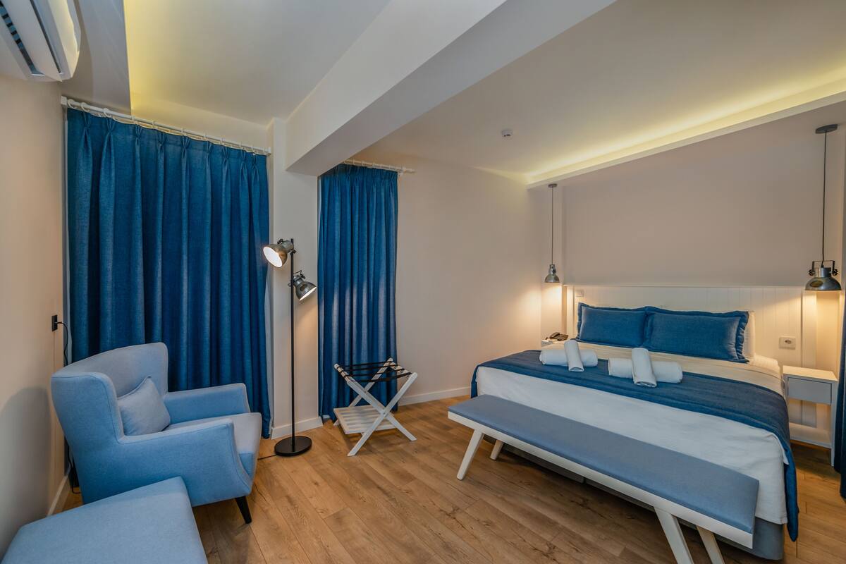 A modern bedroom with a bed, a chair, a bench, a floor lamp, and a small table.