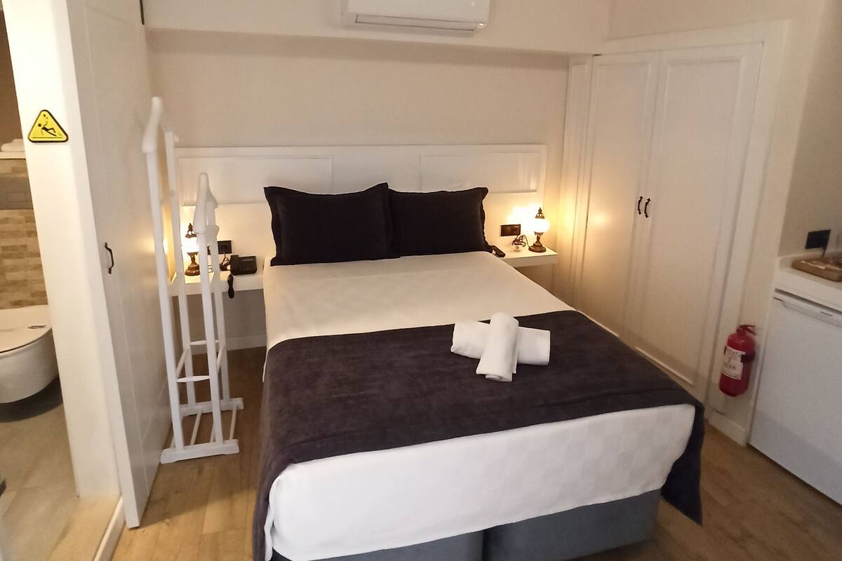 A hotel room with a bed, bedside tables, a wardrobe, and a bathroom visible through an open door.