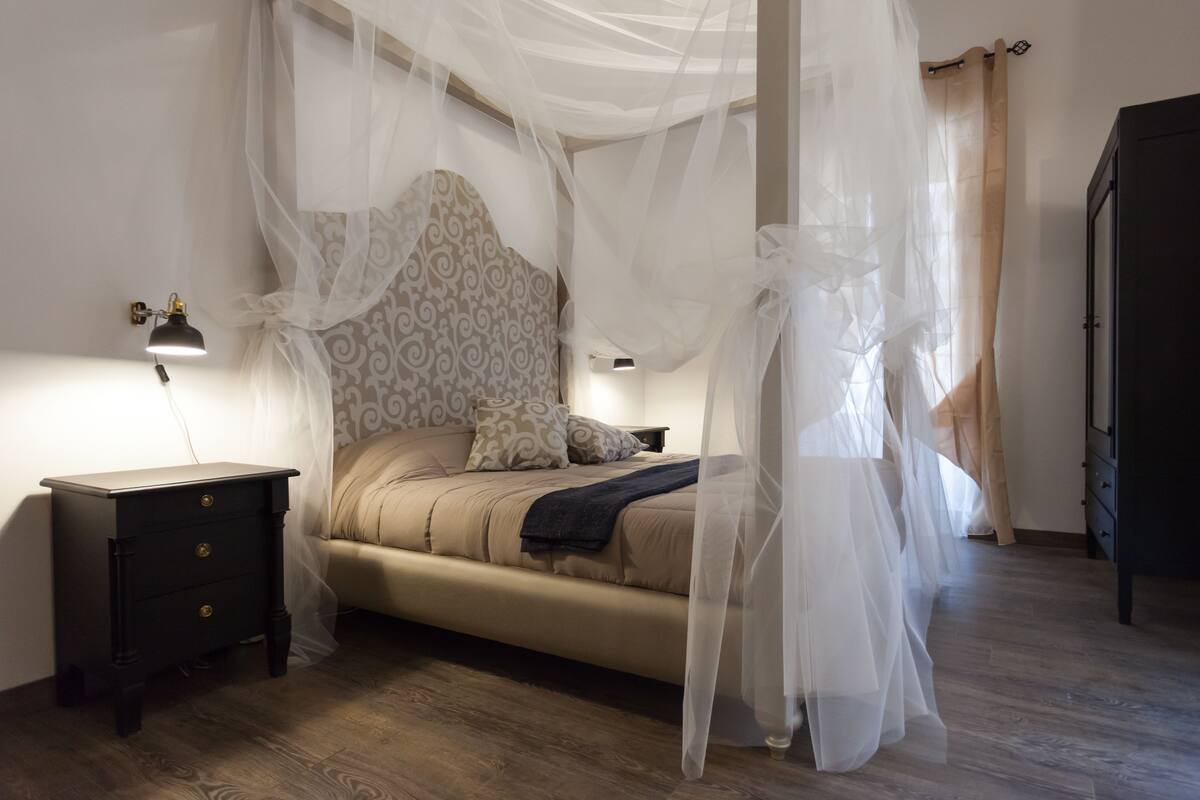 Um quarto com cama, mesa de cabeceira, luminária e guarda-roupa.