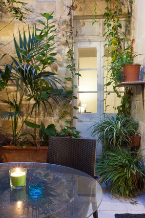 A glass table with a candle and a blue candle holder, surrounded by potted plants and a wicker chair. - Your Apartment Malta (Floriana)