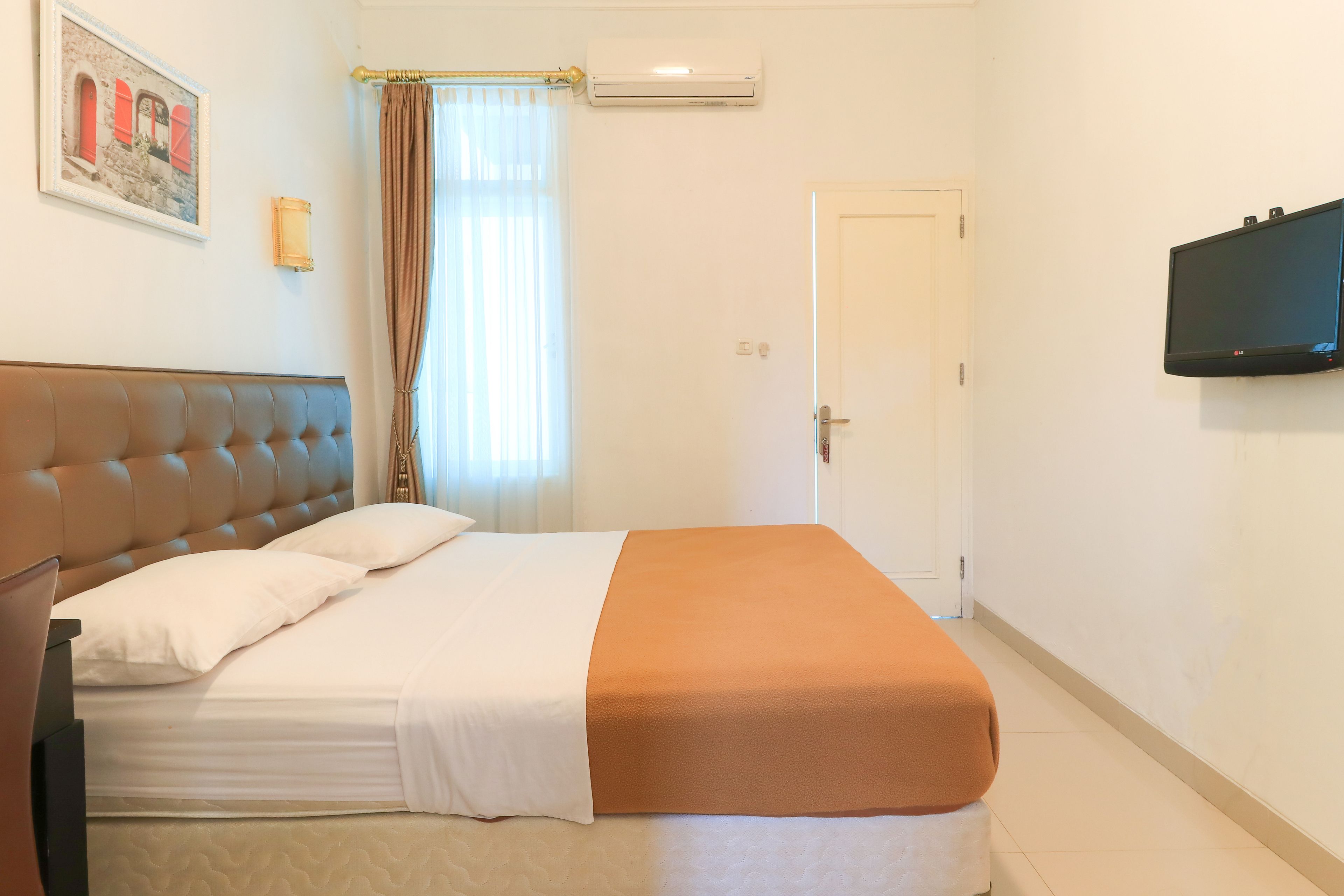 A hotel room with a bed, a television, a door, and a window with curtains.