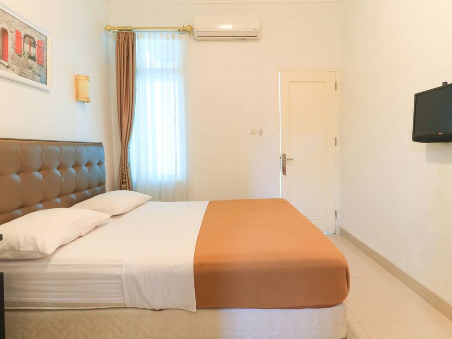 A hotel room with a bed, a television, a door, and a window with curtains.