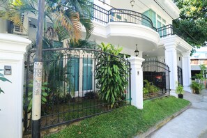 Un bâtiment blanc doté d’un balcon incurvé, d’une clôture en métal et de plantes vertes.
