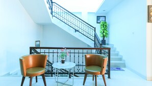 A staircase with a black railing, a potted plant, and two chairs with a small table in the foreground. - Ge JacMart Homestay (Makassar)