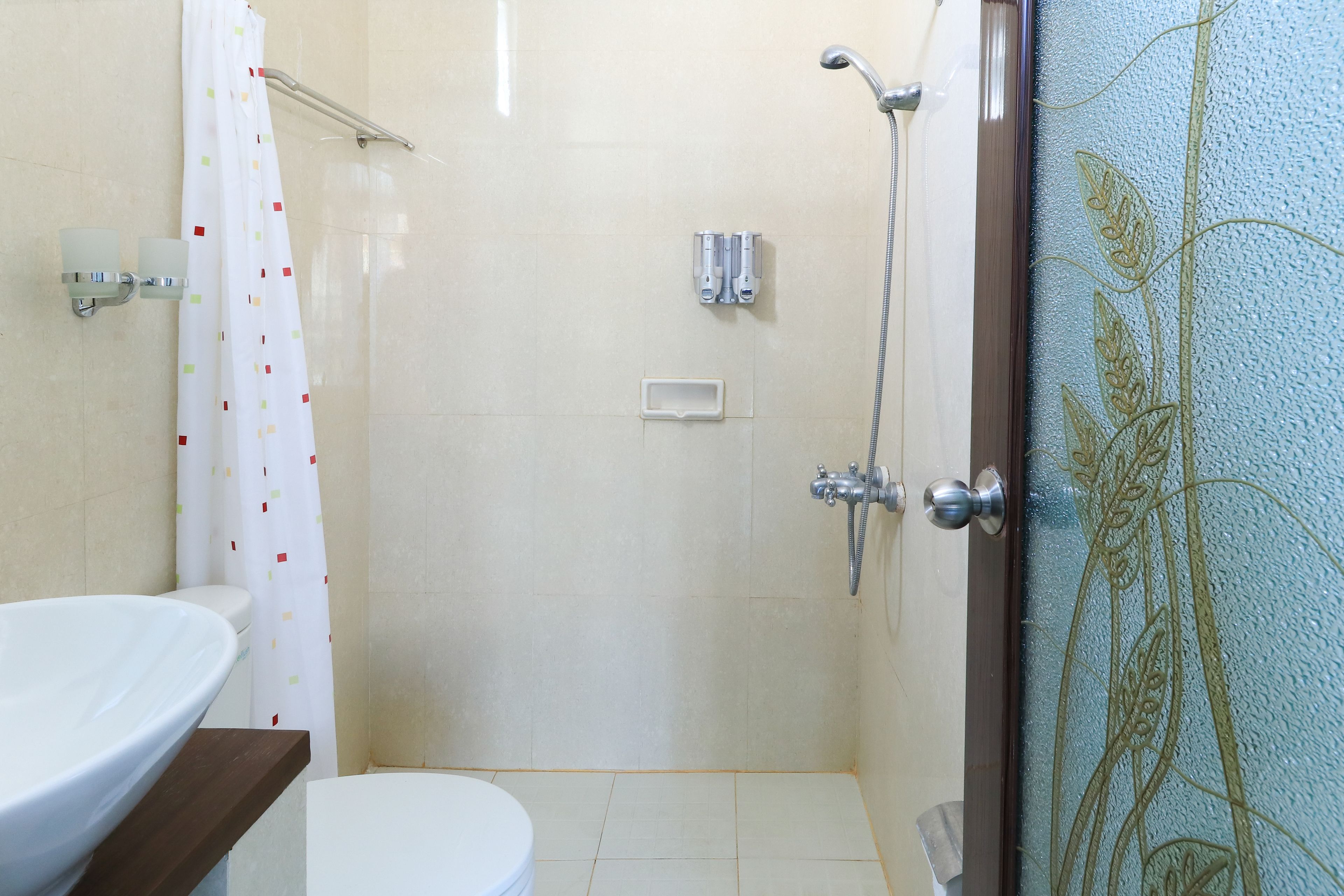 Baño con inodoro, lavamanos, ducha y puerta de vidrio con diseño floral.