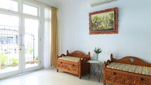 A room with two wooden sofas, a small table with a vase, and a painting on the wall. - Ge JacMart Homestay (Makassar)