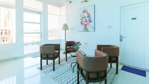A modern waiting area with a reception desk, four brown chairs, a lamp, and a colorful artwork on the wall. - Ge JacMart Homestay (Makassar)