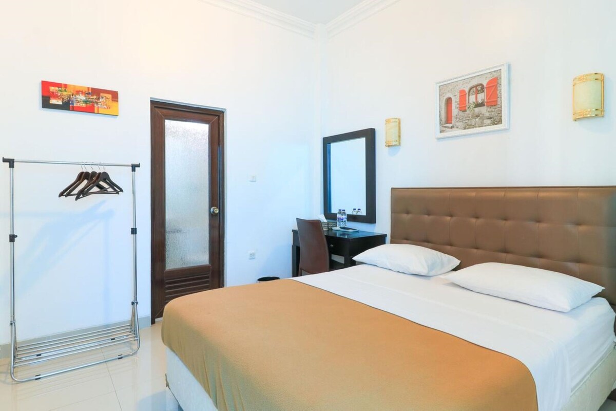 Habitació d'hotel amb llit, escriptori, cadira, armari i mirall.
