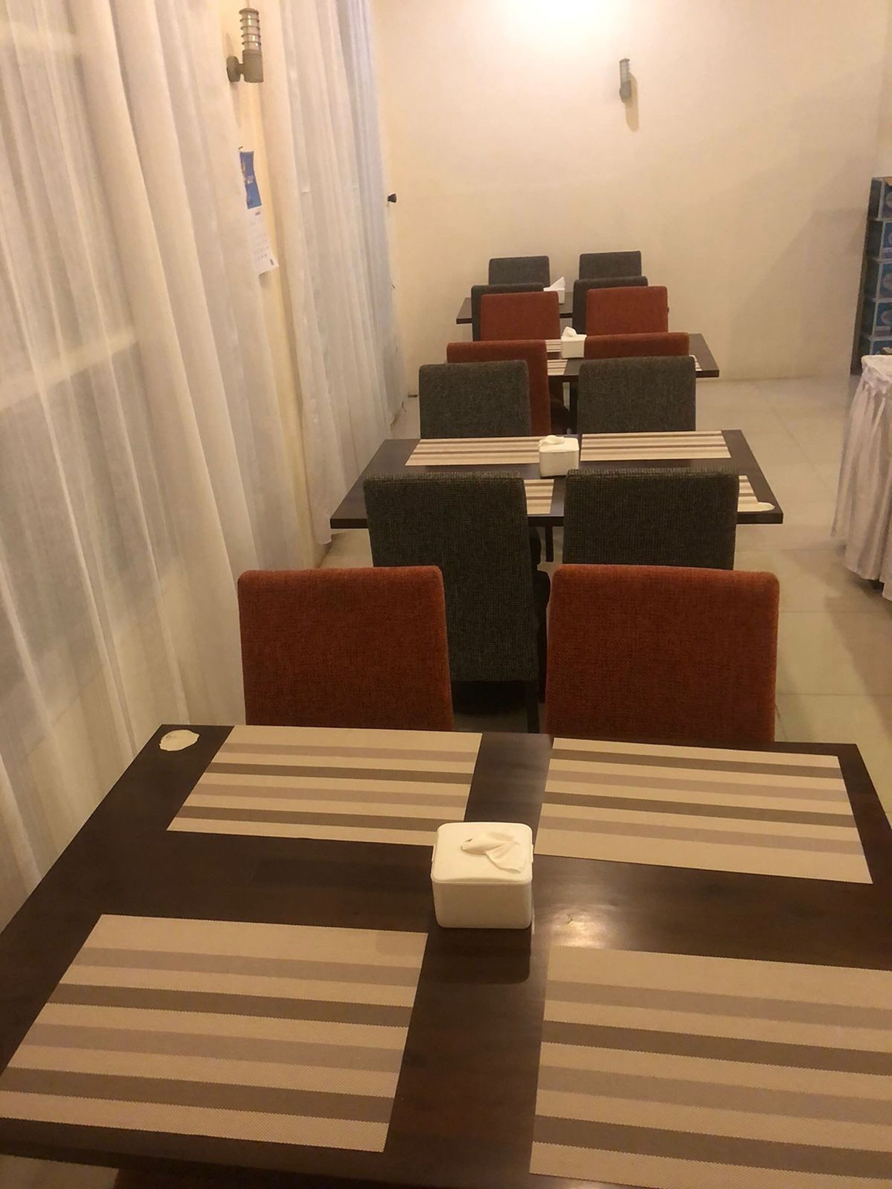 Un espace repas avec des tables et des chaises, une petite table sur laquelle se trouve une boîte de mouchoirs, et un rideau qui recouvre partiellement la fenêtre.