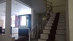 A staircase with metal railings and a handrail, leading to a landing with a white table and chairs. - Hotel Monika (Rantepao)