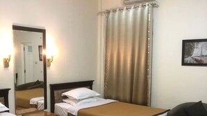 A hotel room with two beds, a chair, a mirror, and an air conditioning unit. - Hotel Monika (Rantepao)